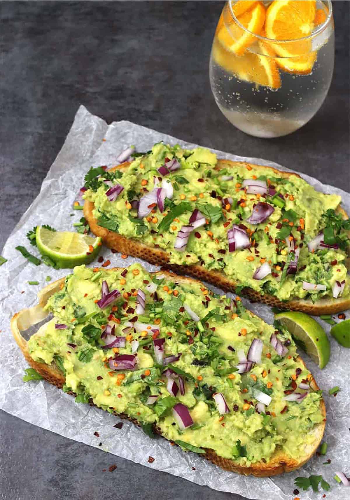 Best guacamole toasts served with sparkling water with orange wedges.