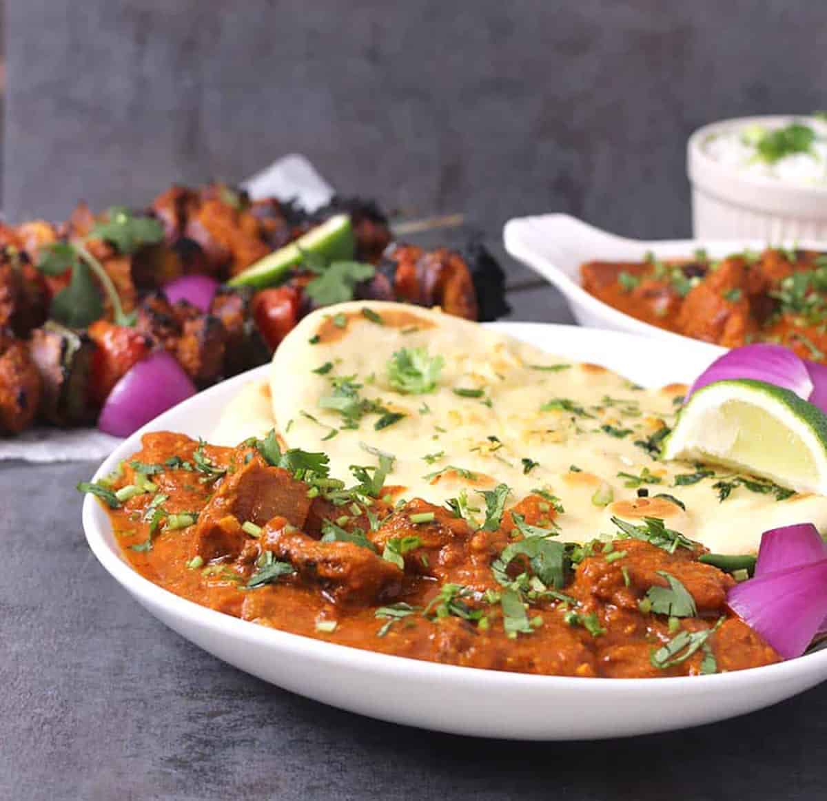 Delicious homemade chicken tikka masala serve in a white plate along with naan bread, red onion slices and a lemon wedge.