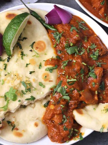 Dhaba-style chicken tikka masala served in a white plate along with naan bread, red onion slices and a lemon wedge.
