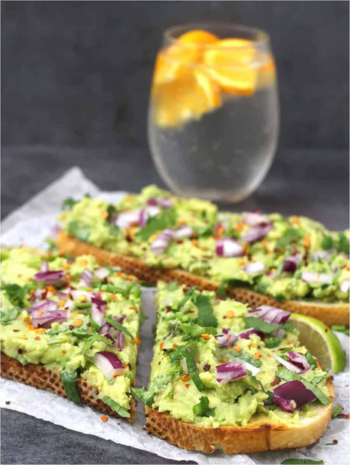 Healthy breakfast toast with mashed avocados, and interesting topping ideas. Sparkling water with orange wedges in the background.