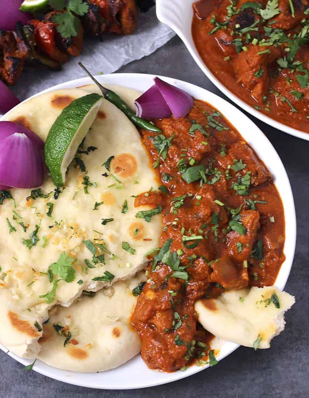 Chicken tikka masala prepared in an Instant Pot served in a white plate along with naan bread, red onion slices and a lemon wedge.