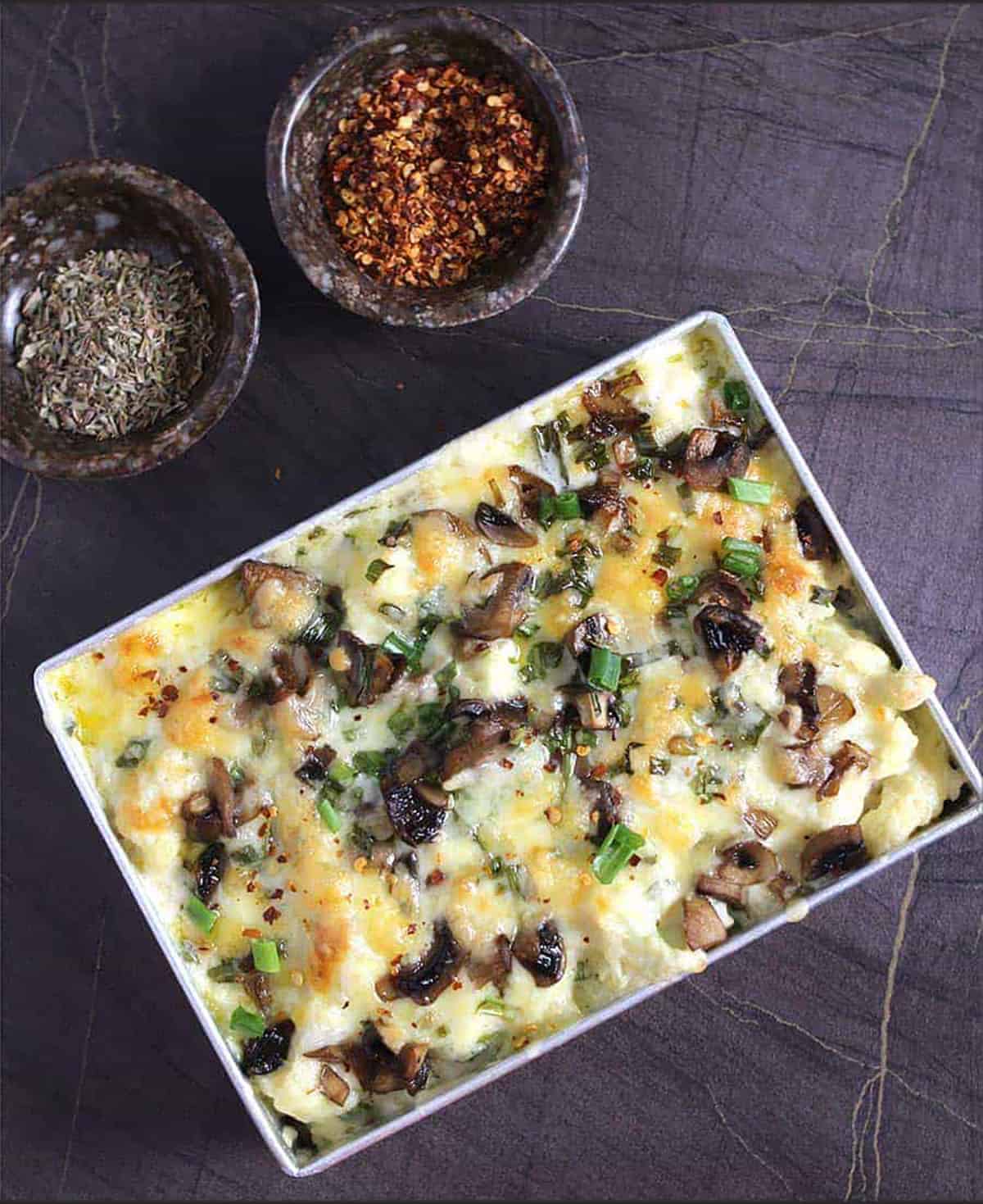 Top view of creamy and cheesy loaded cauliflower casserole with sauteed mushrooms.