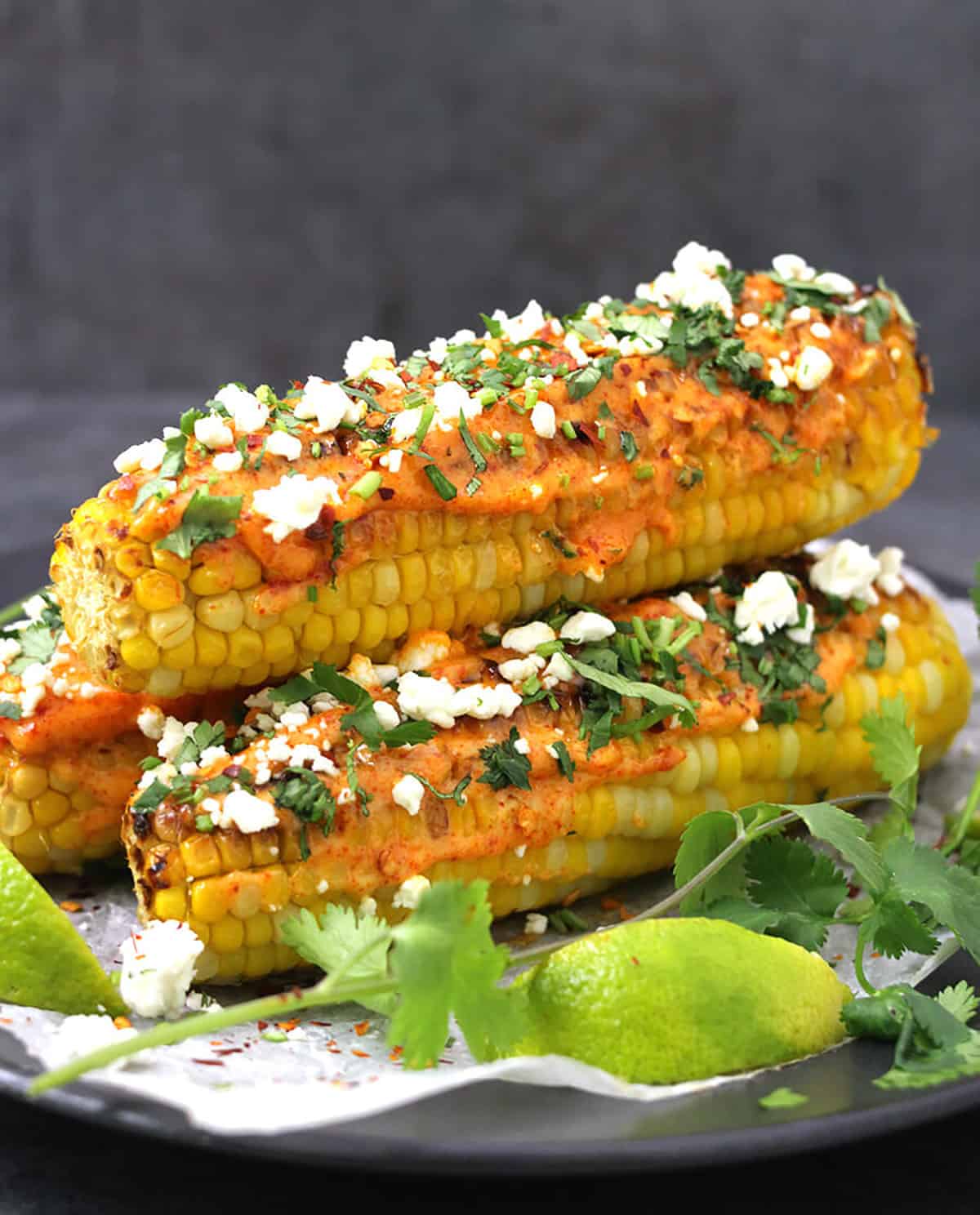Front view of mexican-style corn on the cob served with a drizzle of spicy mayo, cojita cheese, and red pepper flakes.