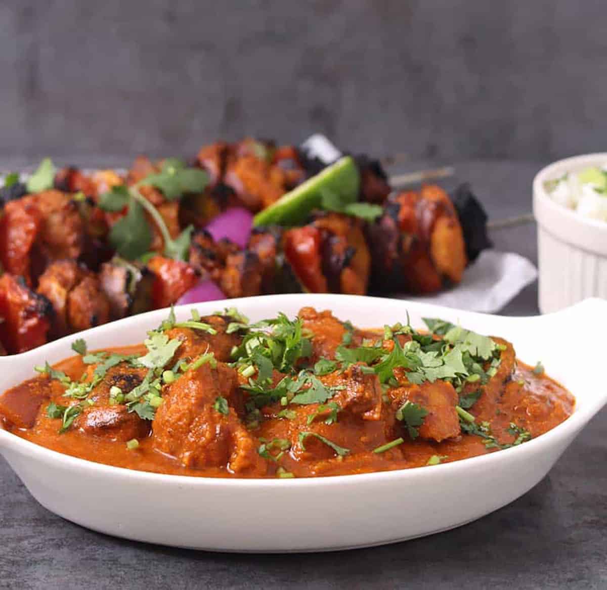 Creamy and spicy murgh tikka masala serve in a white serving bowl and garnished with finely chopped cilantro.