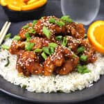 Crispy Orange chicken garnished with spring onions and toasted sesame seeds served over a bed of steamed rice.