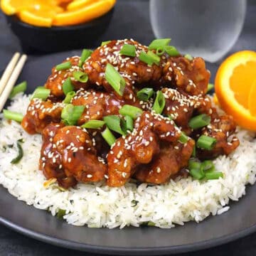 Crispy Orange chicken garnished with spring onions and toasted sesame seeds served over a bed of steamed rice.