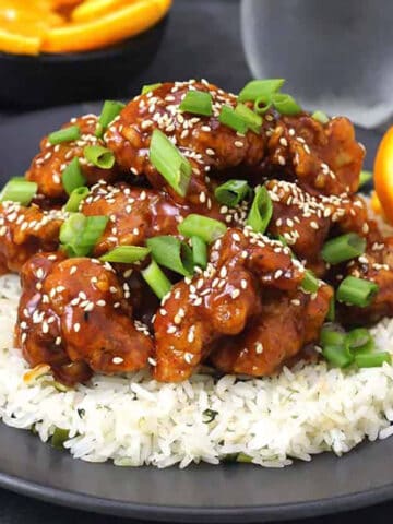 Crispy Orange chicken garnished with spring onions and toasted sesame seeds served over a bed of steamed rice.