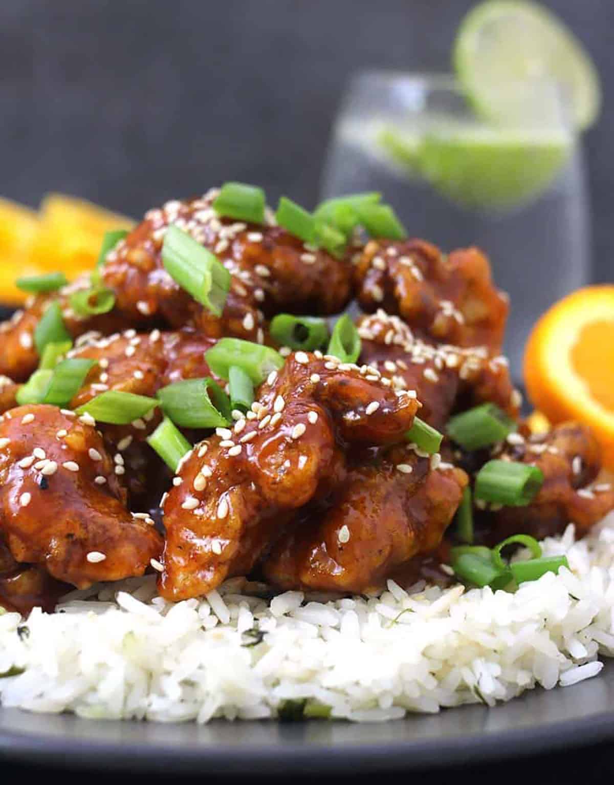 Orange chicken garnished with scallions and toasted sesame seeds served over a bed of steamed rice.