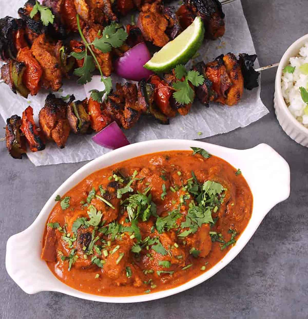 Top view of punjabi chicken tikka masala serve in a white serving bowl. Skewers of chicken tikka in the background.
