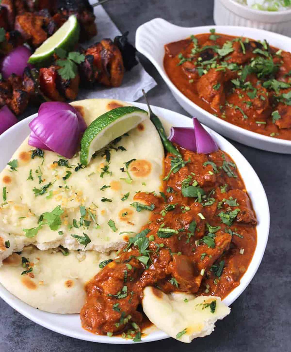 Restaurant-style chicken tikka masala serve in a white plate along with naan bread, red onion slices and a lemon wedge.