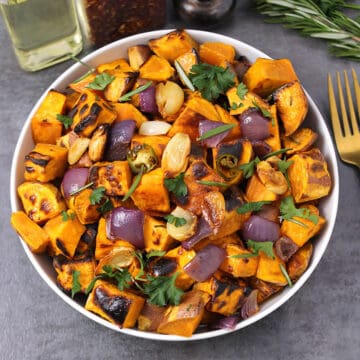 Roasted sweet potatoes garnished with fresh cilantro and presented in a white bowl.