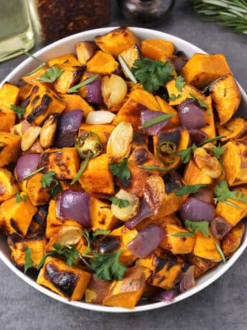 Roasted sweet potatoes garnished with fresh cilantro and presented in a white bowl.