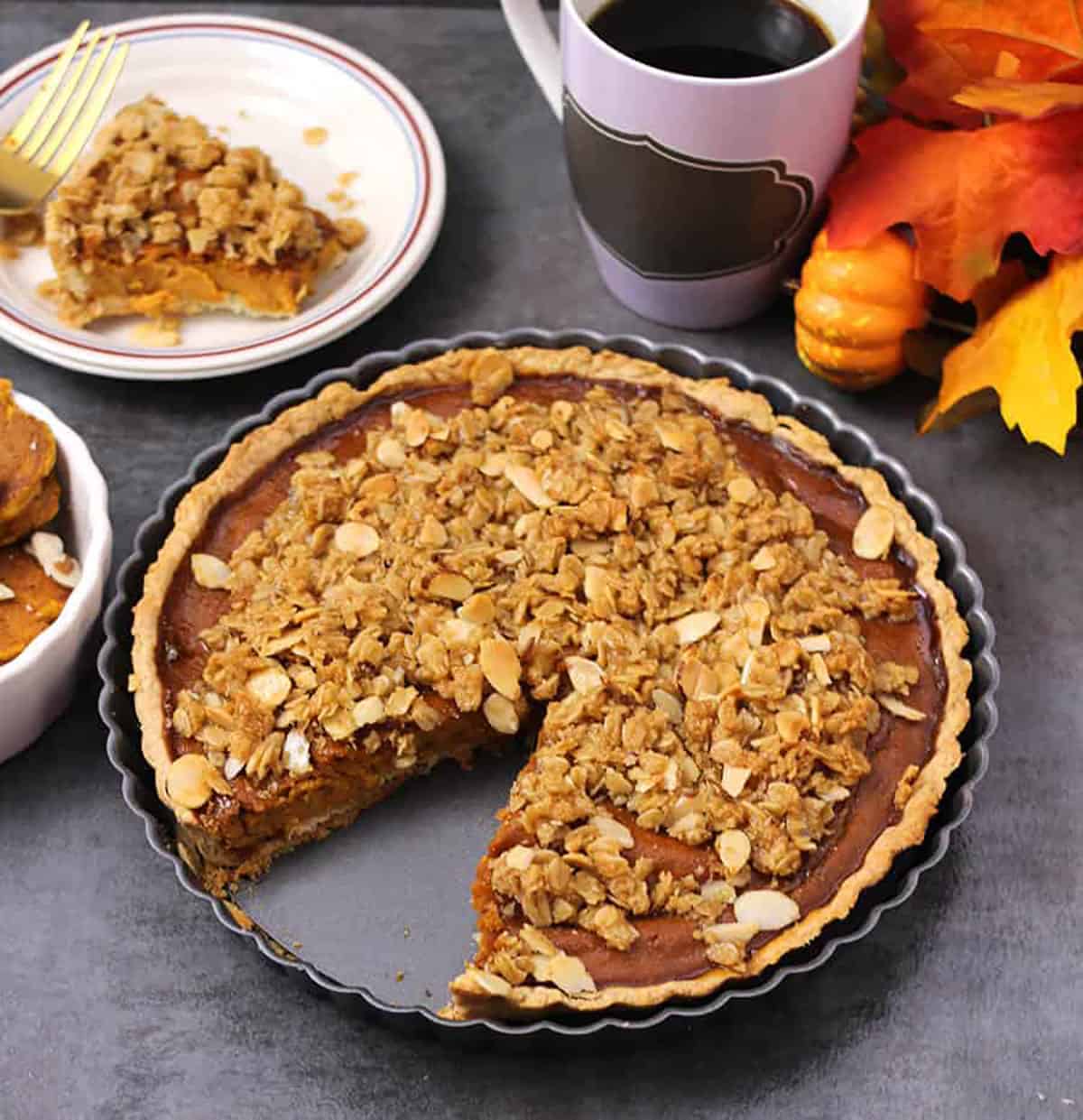 pumpkin pie with streusel topping. with a slice served in a plate along with black coffee.
