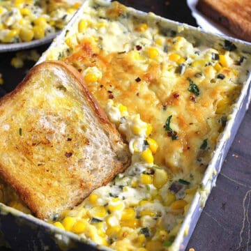 cheesy corn casserole served in a baking pan along with a slice of toasted bread.