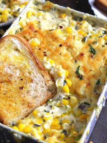 cheesy corn casserole served in a baking pan along with a slice of toasted bread.
