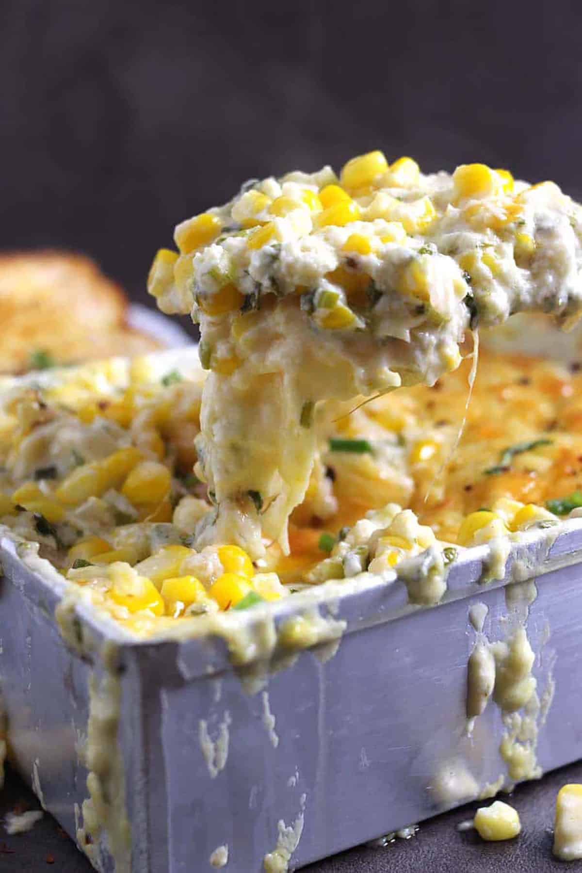 cheesy corn casserole being served from the baking pan using a wooden spatula.