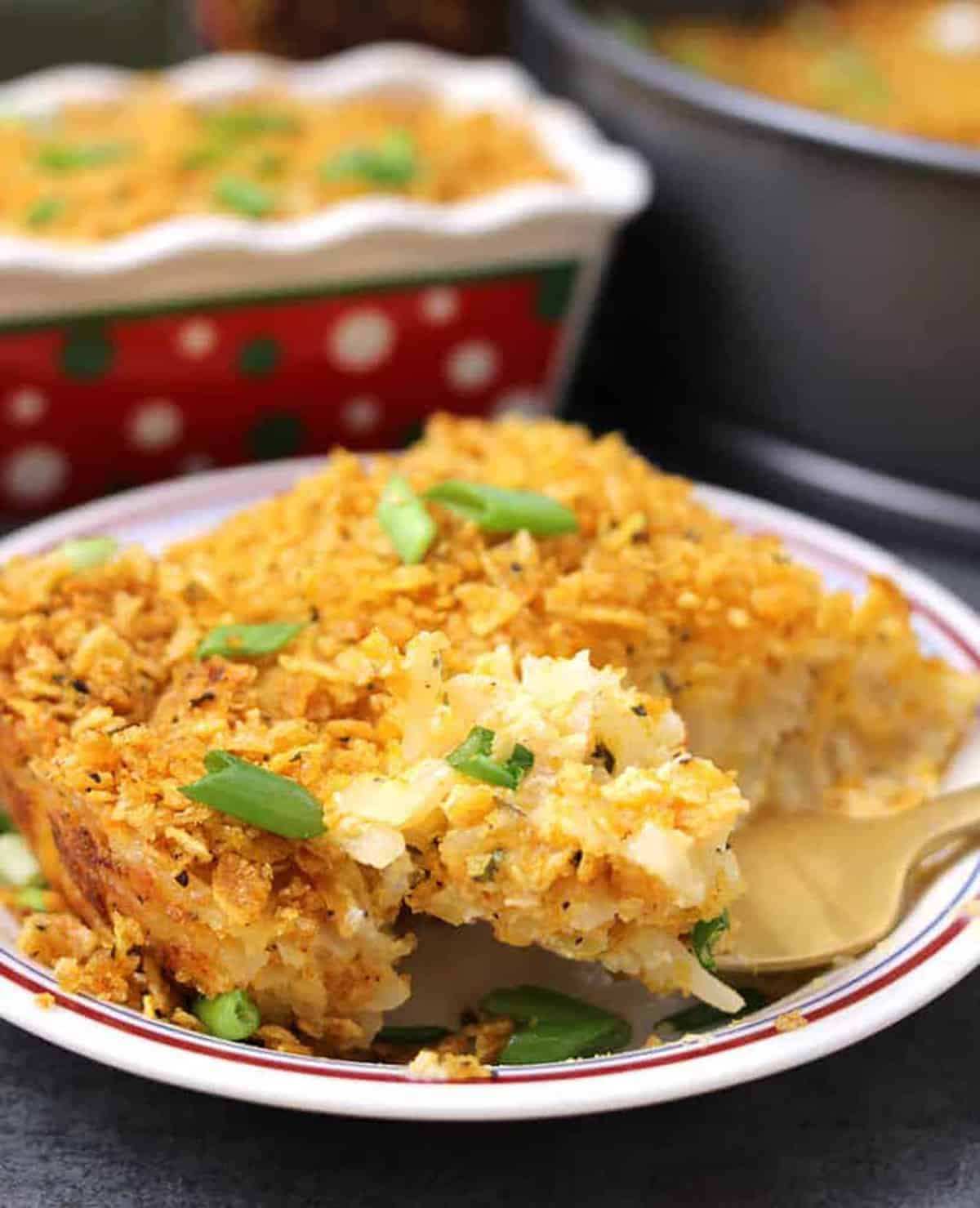 creamy and cheesy potato casserole with crispy cornflake topping served in a white appetizer plate.