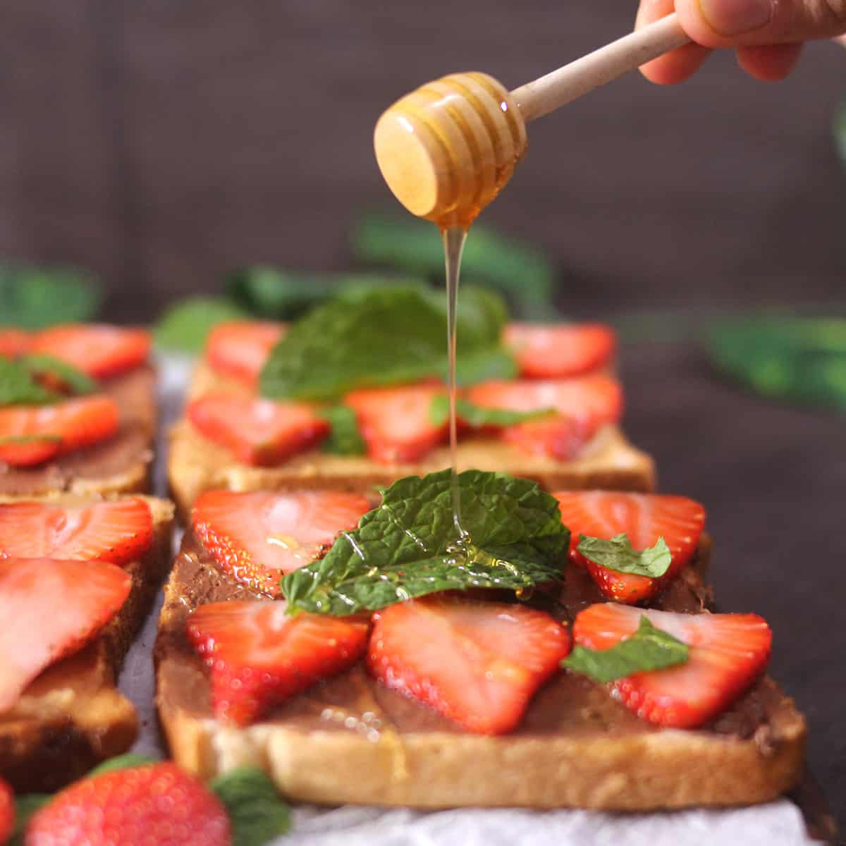 Drizzle honey on the strawberry bread toast using a wooden honey dipper.
