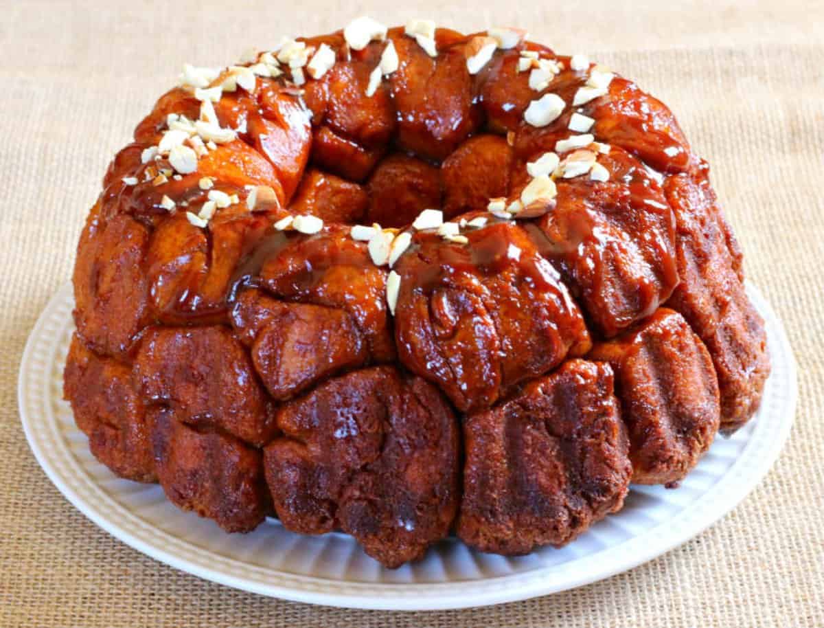 Moist and gooey monkey bread garnished with nuts and served in a white ceramic plate.