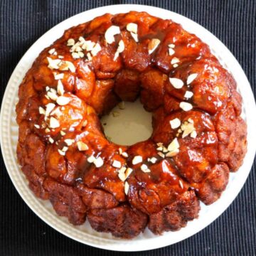 Pull apart classic monkey bread garnished with nuts served in a white ceramic plate.