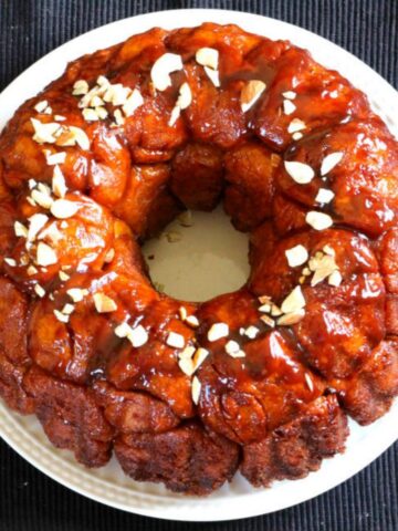 Pull apart classic monkey bread garnished with nuts served in a white ceramic plate.