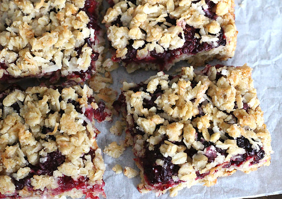 blackberry jam/preserves oatmeal breakfast bars with crunchy crumbly topping on parchment paper.
