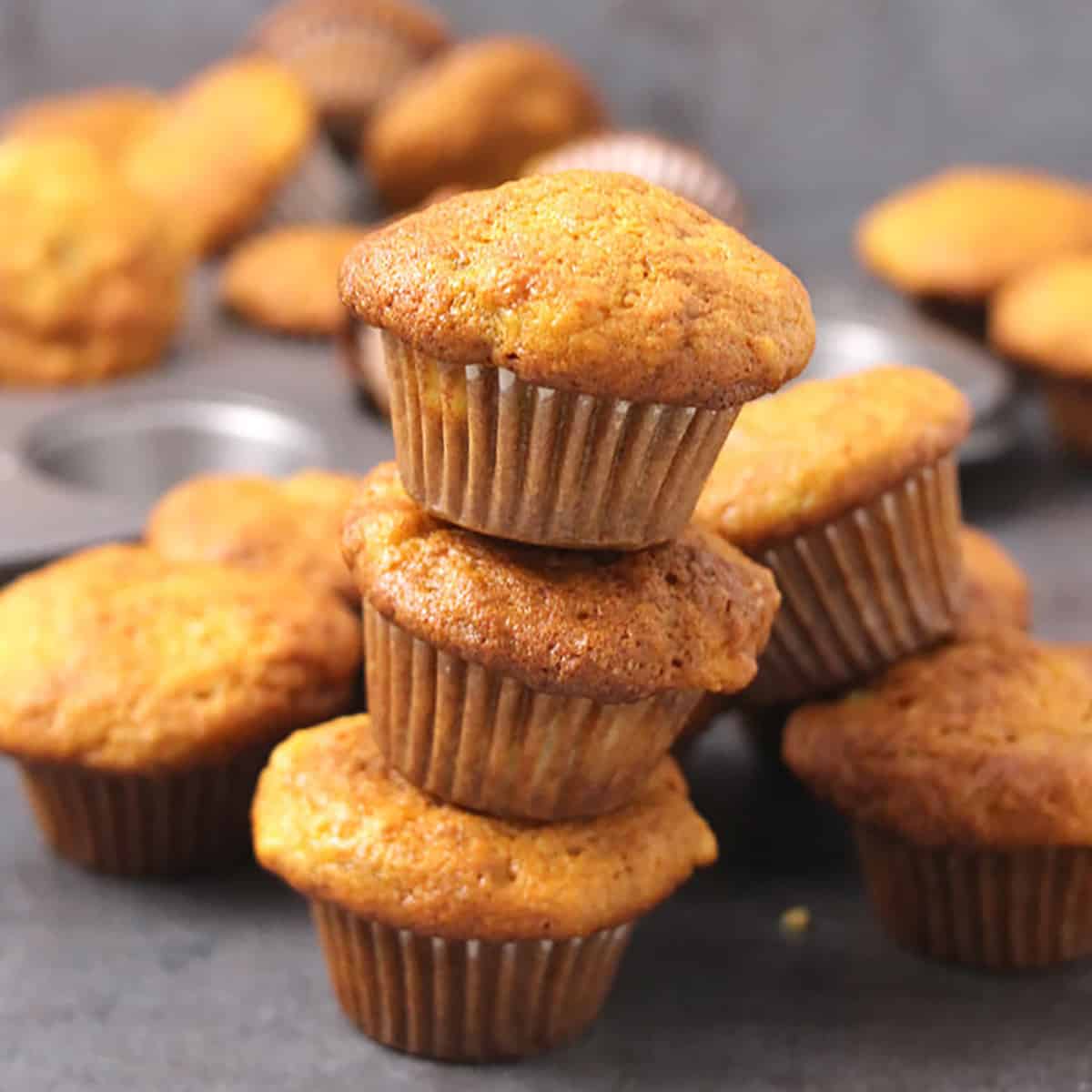 moist banana muffins stacked on each other, with many in the background.