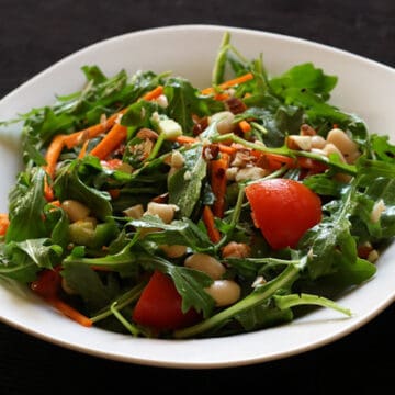 Arugula salad with white beans in lemony dressing served in a white plate.