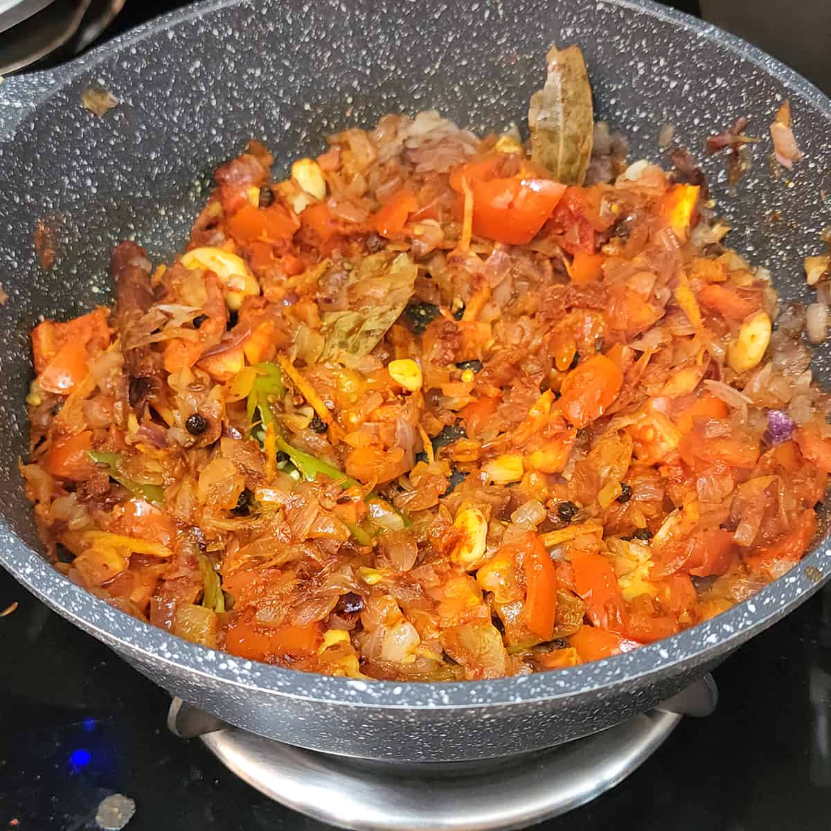 Cooked onions and tomatoes along with whole spices and spice powders in a nonstick pan.