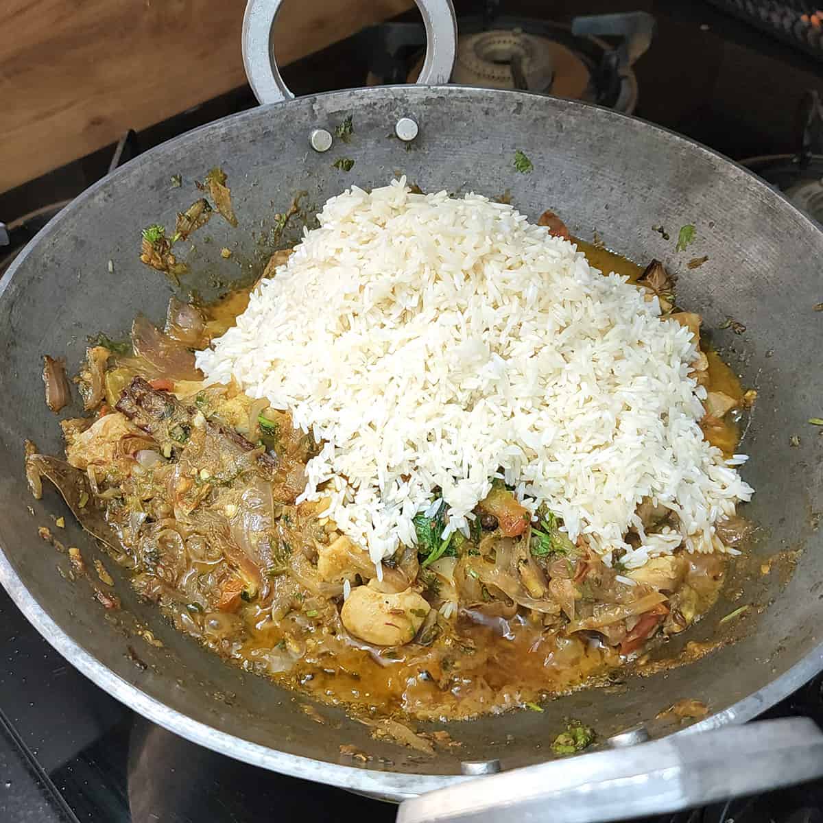 Adding soaked and drained basmati rice to the pan in which spiced chicken pilaf is made.