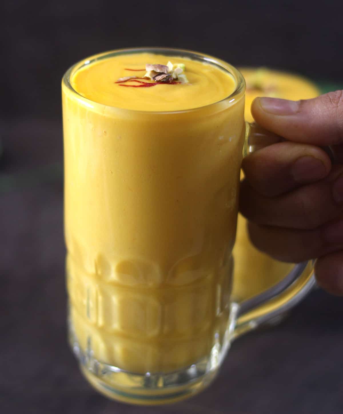 Holding a glass of thick and creamy mango smoothie lassi drink. 
