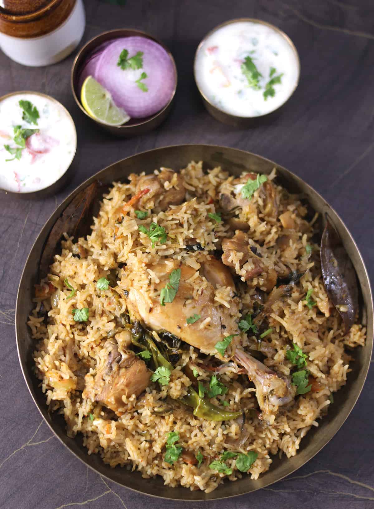 Best and easy chicken pulao (pilau) served in a bronze plate with raita (yogurt salad) and onions. 