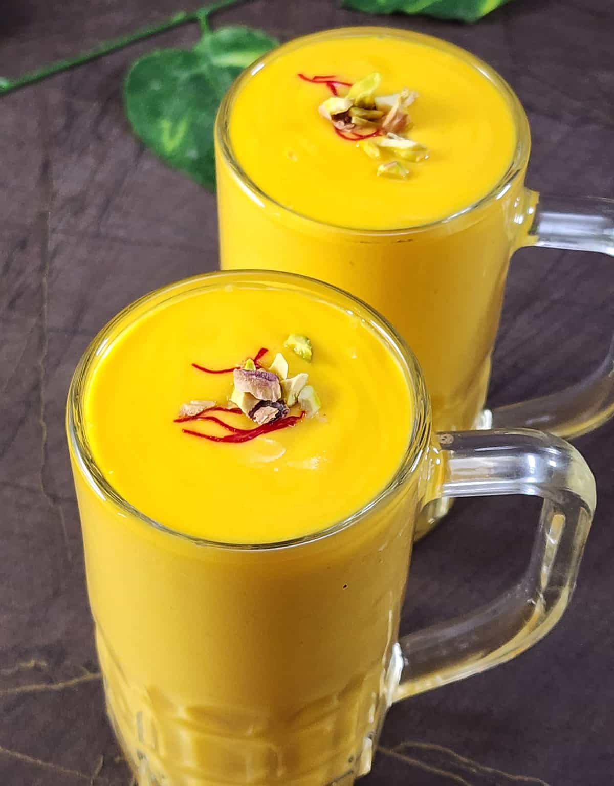 Two glasses of best mango lassi or mango smoothie garnished with saffron and chopped pistachios.