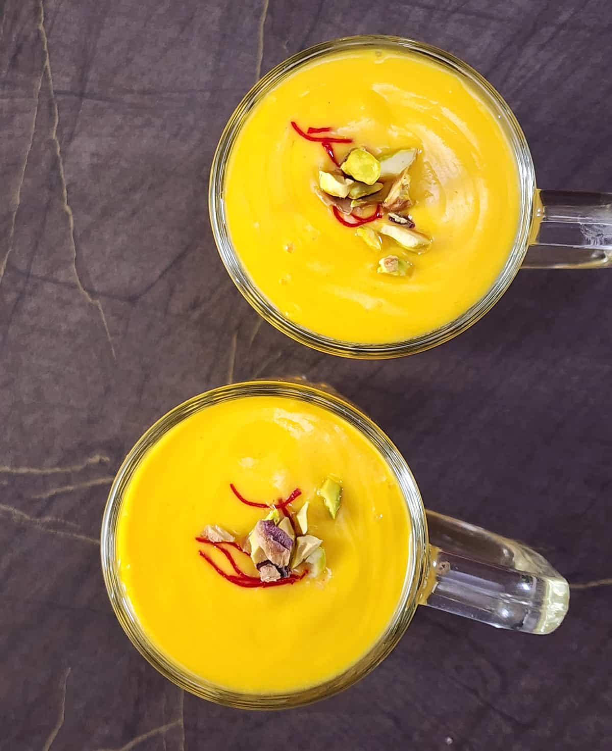 Top view of traditional mango smoothie or lassi garnished with pistachio and saffron and served in glass mugs. 