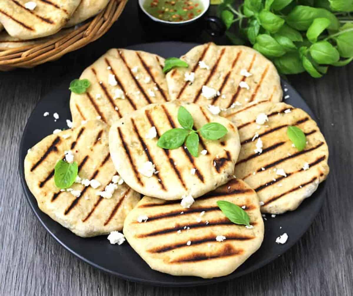 Grilled mini flatbreads that are stuffed with feta cheese and olives are served in a black plate.