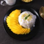 Easy Thai Mango sticky rice dessert on a black plate topped with salted coconut sauce and mung beans.