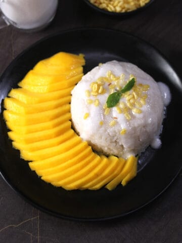Easy Thai Mango sticky rice dessert on a black plate topped with salted coconut sauce and mung beans.