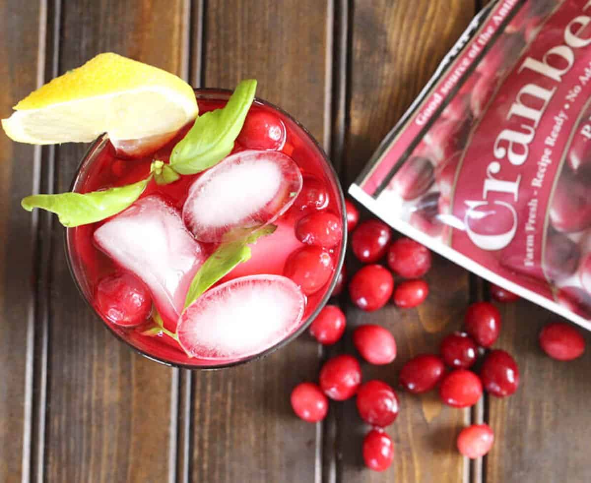 Quick and Easy cranberry lemonade with real cranberries served in a glass filled with ice and garnished with a slice of lemon and mint leaves.
