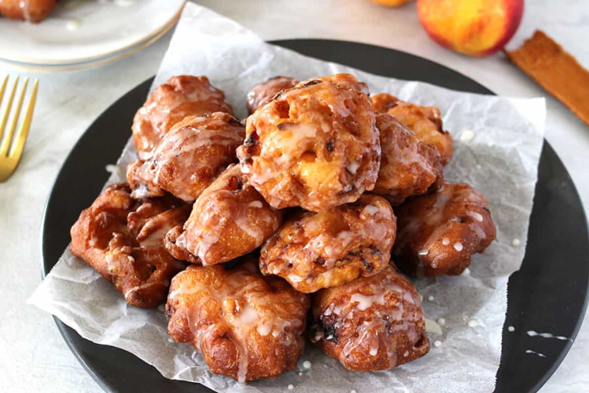 Freshly prepared peach fritters with simple sugar glaze served in a black plate.