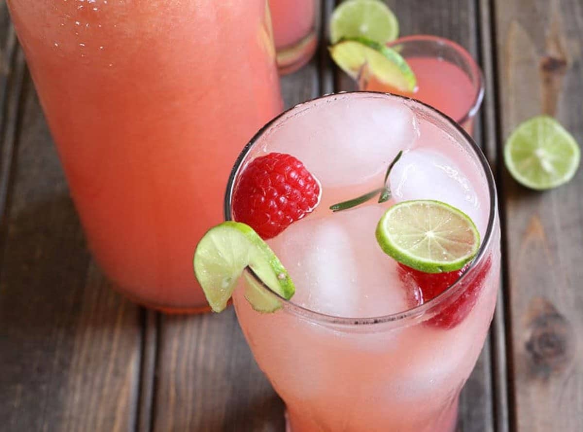 Delicious pink lemonade served in a tall glass with ice cubes, whole raspberries, and lemon slices.