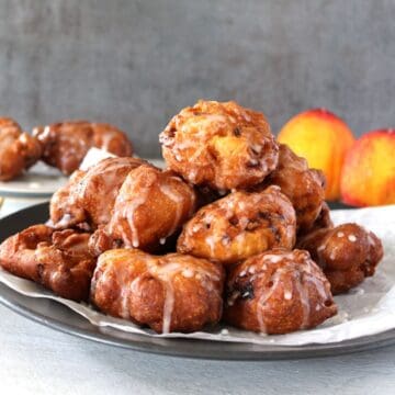 A Pile of Homemade Peach Fritters on white parchment paper, drizzled with sugar glaze.