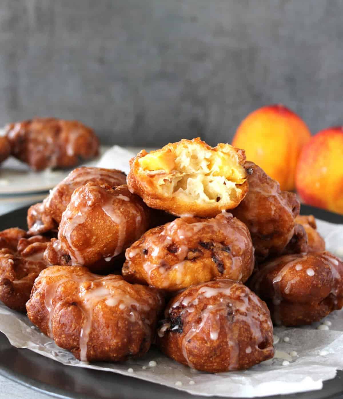 Quick and easy peach fritters served on a black plate. The fritter on top is opened to show the delicate and fluffy interior.