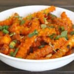 Saucy potato fries garnished with cilantro and spring onions, and served in white ceramic bowl.