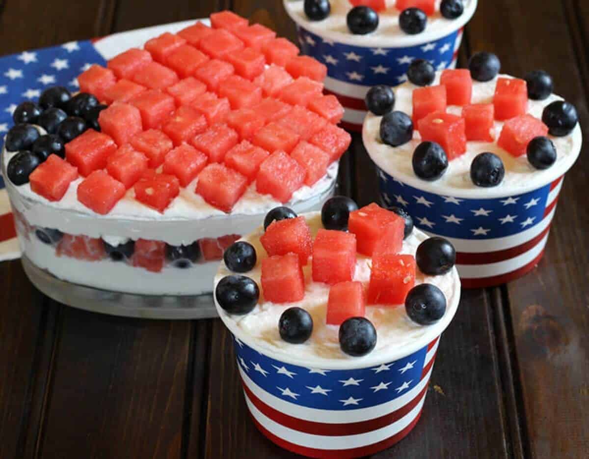 Quick and Easy fruit salad with cream served in American Flag themed paper ice cream cups. Watermelon cubes and blueberries are arranged as stripes and stars on the top.