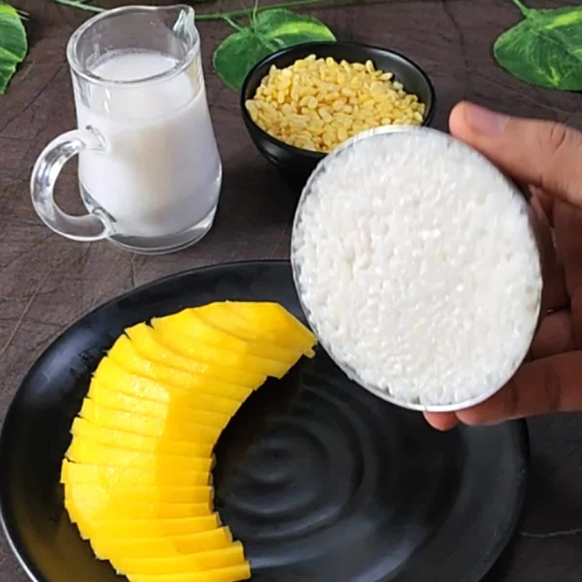 Transfer a small bowl of sticky rice to a black plate containing sliced mangoes. 