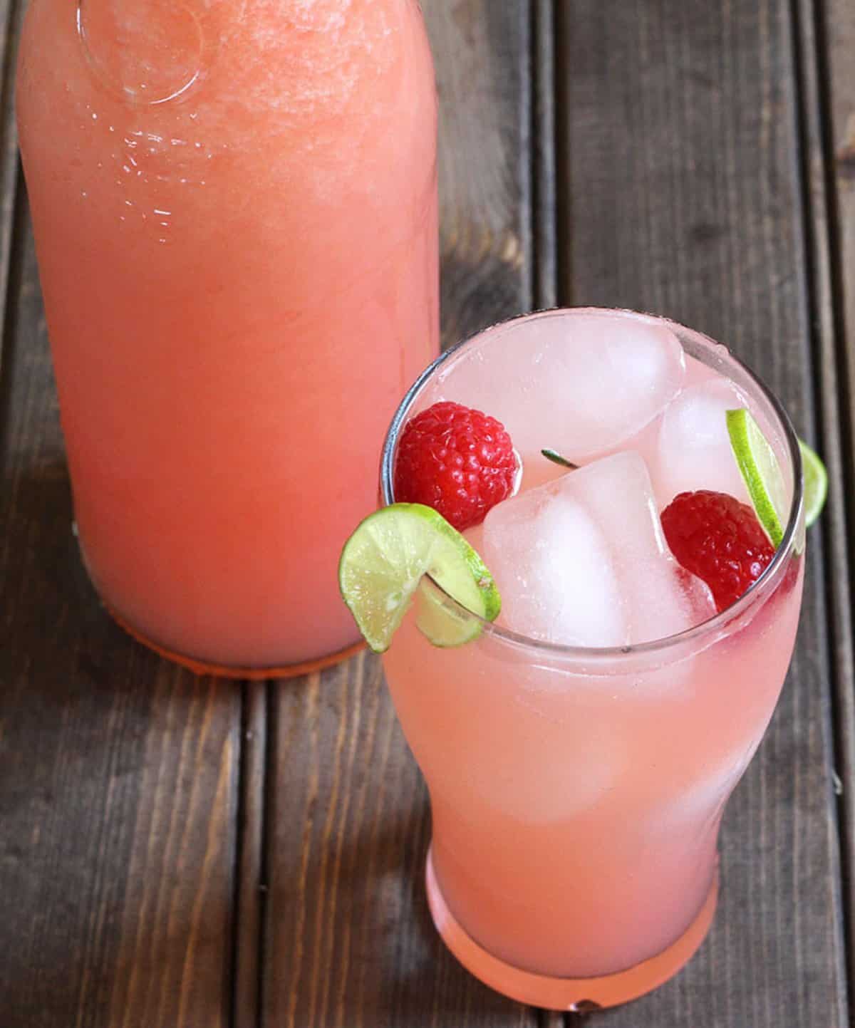 Raspberry Lemonade summer drink served with ice cubes, whole raspberries, and lemon slices in a tall glass.