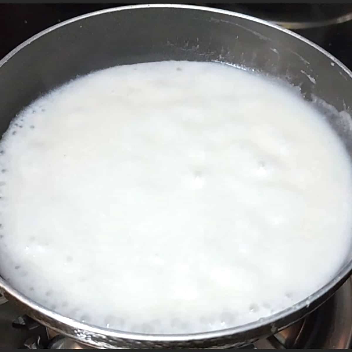 Simmer salted coconut sauce in a black nonstick pan.