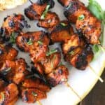 Delicious Chicken Satay Skewers served in a white plate along with a garnish of cilantro.