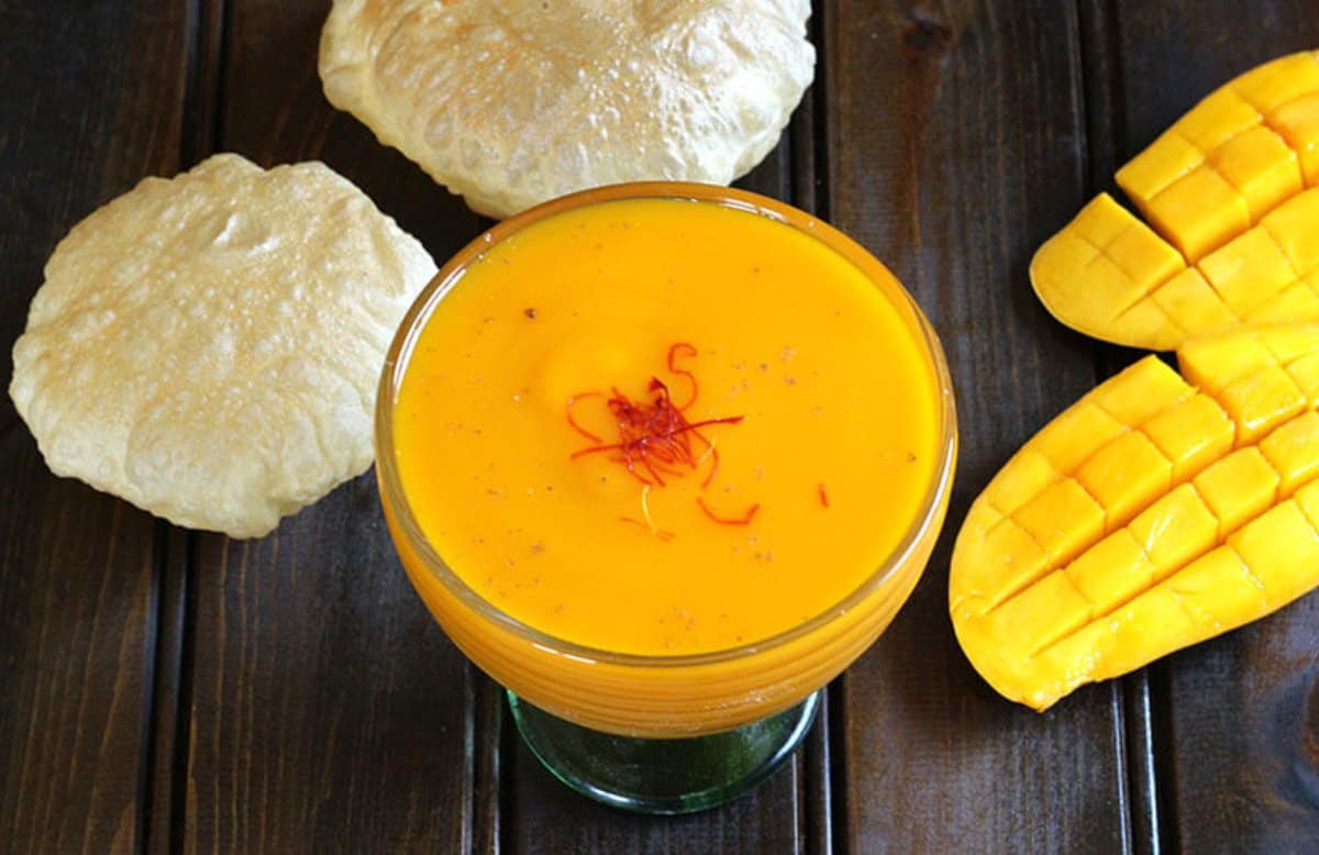 Quick and easy Aamras or Flavored Sweet Mango Puree served in a glass bowl and garnished with saffron. They are served with hot Indian puffed bread called puri or bhatura.
