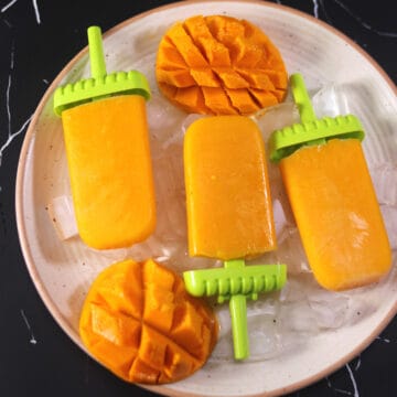 simple and easy homemade mango popsicles on a serving plate with ice cubes and fresh mango slices.